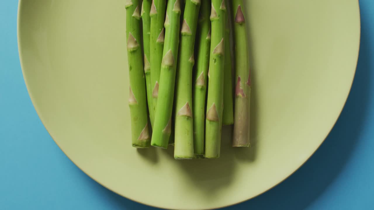 video de espárragos frescos en un plato verde sobre un fondo azul