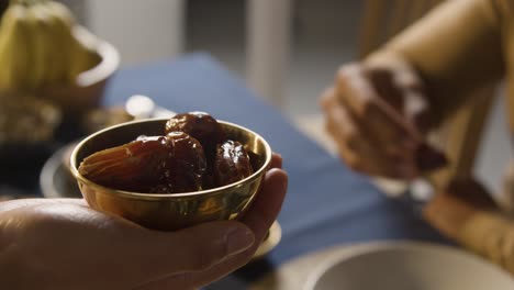 persona que ofrece dátiles en la mesa familiar musulmana en casa preparada para la comida iftar rompiendo el ayuno diario durante el ramadán