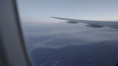 calm view from airplane window showing wing over landscape, blue hues