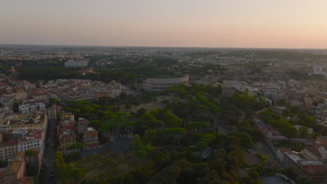 Vorwärts-Fliegen-über-Den-Oppian-Hill-Park-Mit-Historischen-Wahrzeichen.-In-Richtung-Des-Antiken-Amphitheaters-Kolosseum.-Panoramablick-Auf-Die-Stadt-In-Der-Abenddämmerung.-Rom,-Italien