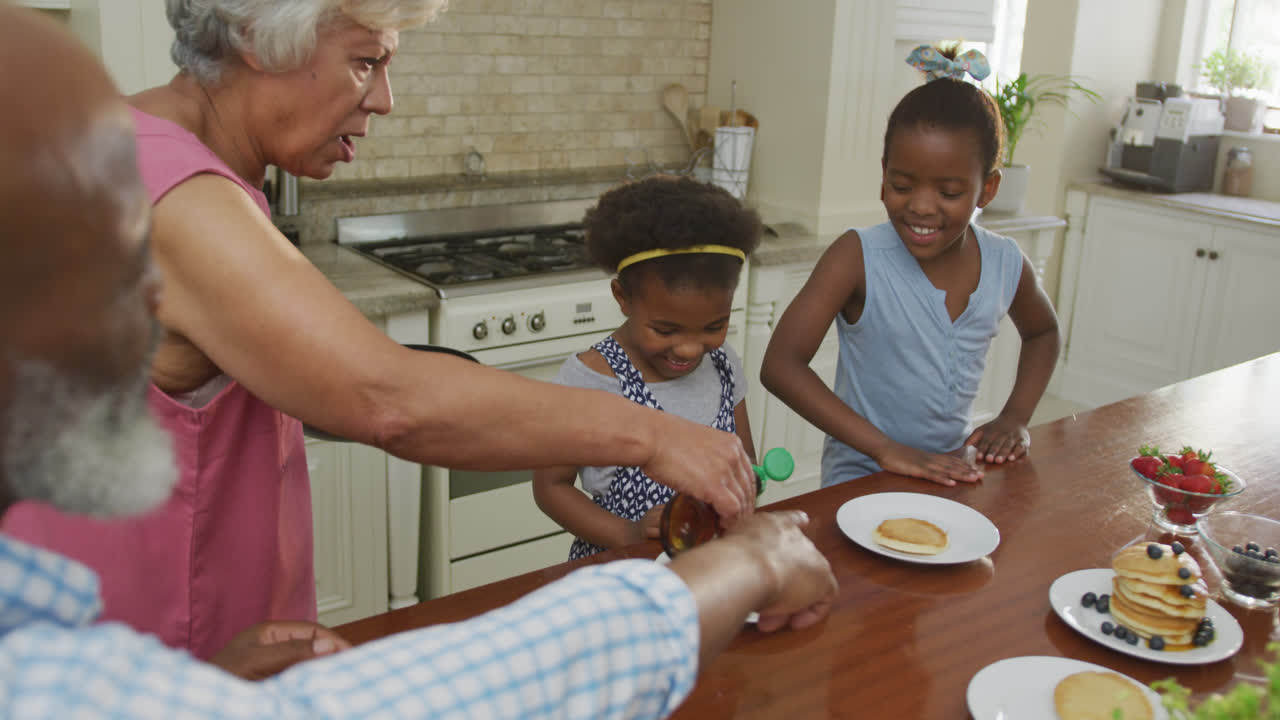 abuelos afroamericanos felices con nietas desayunando y hablando