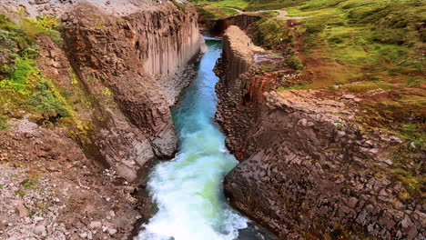 flight above the narrow river flowing among the columnar rocks. tourists walk by the mountainous landscape if iceland. aerial view.