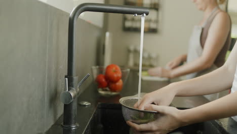 madre e hija están preparando una ensalada en la cocina. en primer plano, las manos están lavando una ensalda, en la parte de atrás, una mujer las corta en una tabla de cortar