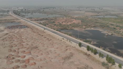 drone pans to the left to get an aerial photo of a car travelling along a roadway near khairpur, sindh, pakistan