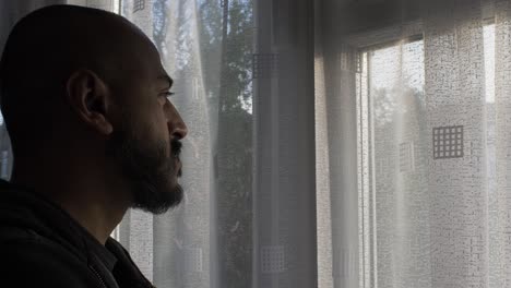 ethnic uk asian male looking out of window in pensive mood during locked down