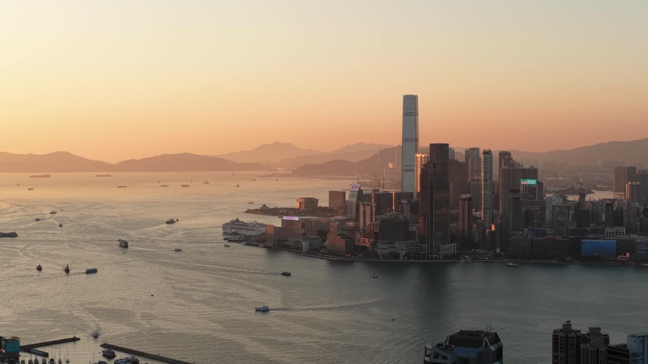 Luftdronevideo af Hongkongs skyline ved solnedgang i den gyldne time, med oplyste højhusbygninger, varme bylys, dramatisk himmel og det tætte bylandskab i en global megaby.