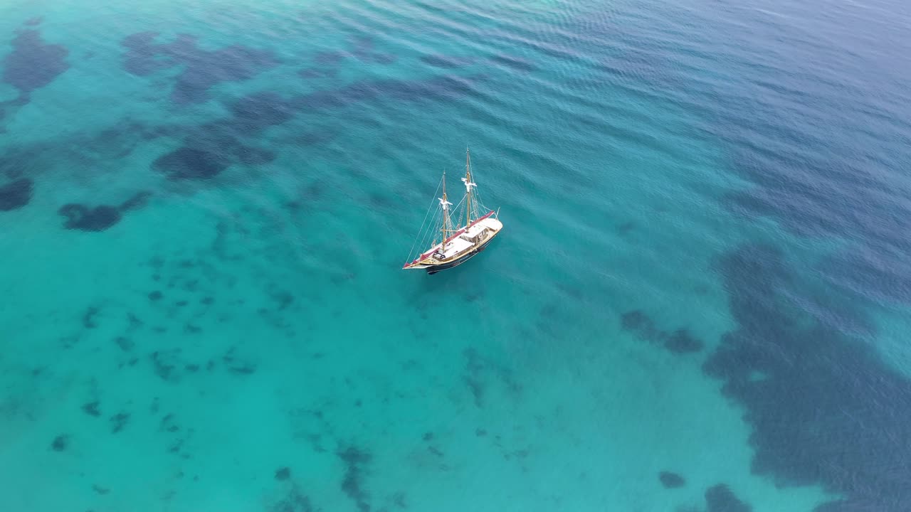 un velero de madera en un mar azul claro en las cícladas, grecia, vista aérea de un avión no tripulado
