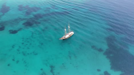 Wooden-sailboat-on-a-clear-blue-sea-in-the-Cyclades,-Greece,-drone-aerial-view