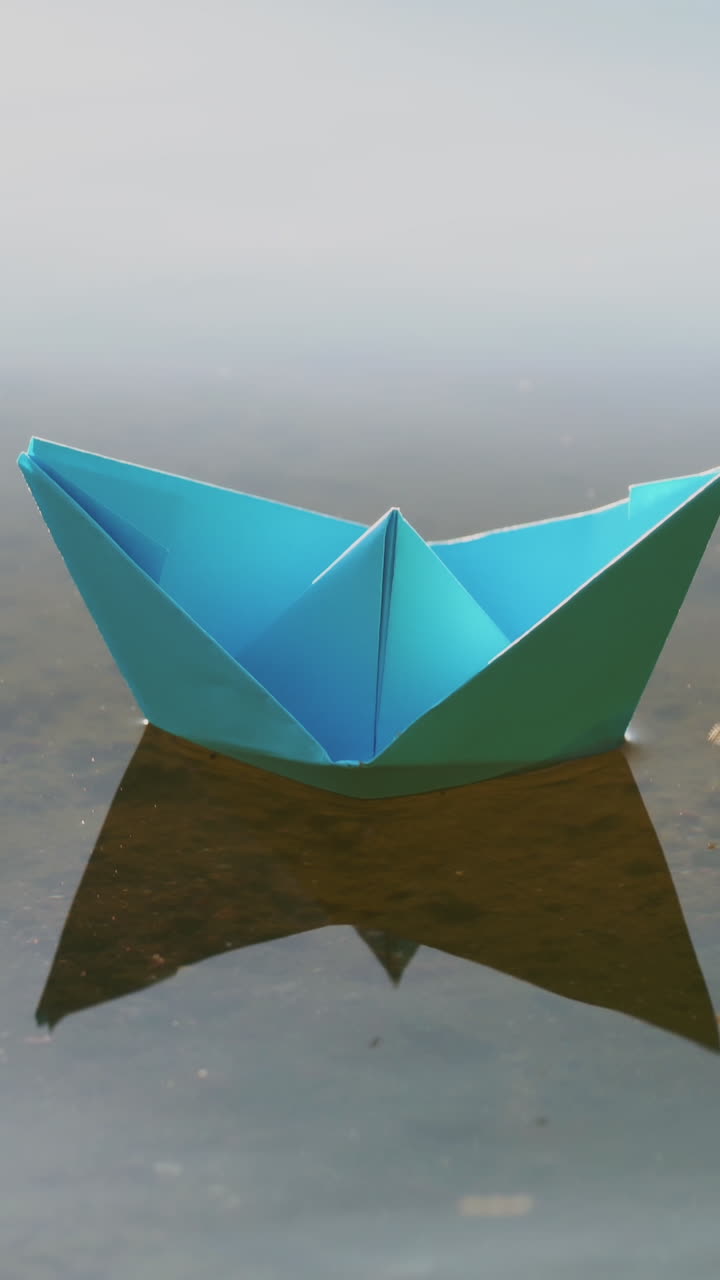 Blue paper boat sailing on water on romantic sunset. Origami. Vertical video
