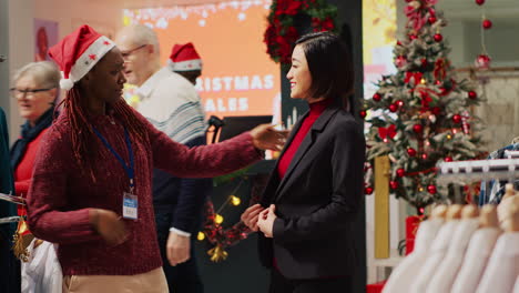 customer happy with perfectly fitting elegant blazer after trying it on, asking worker for opinion in christmas decorated fashion store. retail assistant helping client in xmas ornate clothing shop