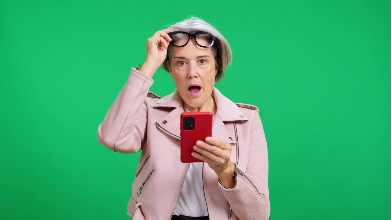 Shocked mature woman looking at smartphone on green screen