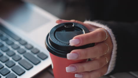 close-up of a woman's hand gently turning a coffee cup near a laptop, focusing on her manicured fingers against a blurred keyboard background