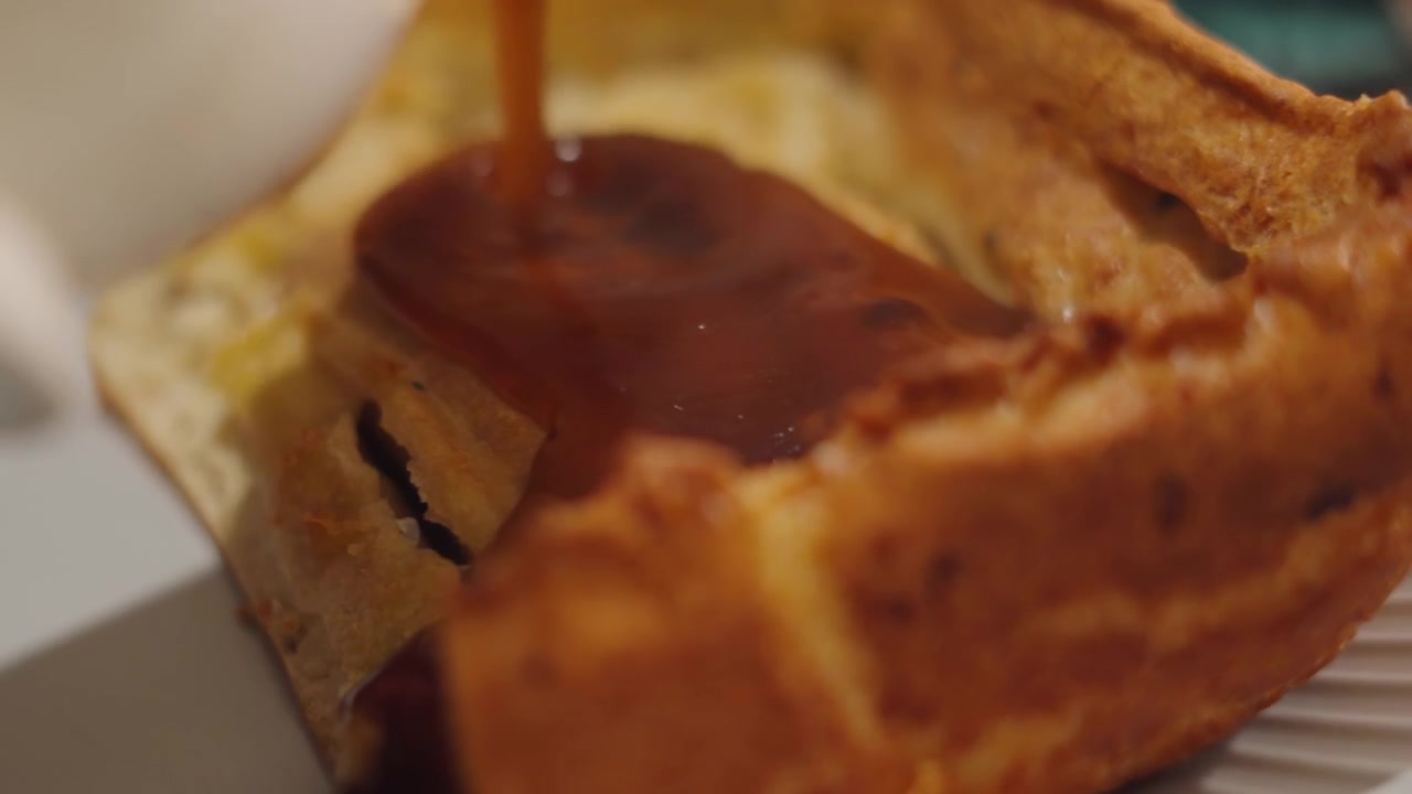 Vista laterale di sugo versato da una brocca su Yorkshire Pudding Toad in the Hole con salsicce di maiale. Cibo consumato a tavola. Piatto tradizionale classico britannico
