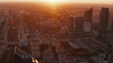 Forwards-fly-above-large-city.-Tilt-up-reveal-of-bright-sky-with-setting-sun.-Silhouettes-of-high-rise-buildings.-Warsaw,-Poland