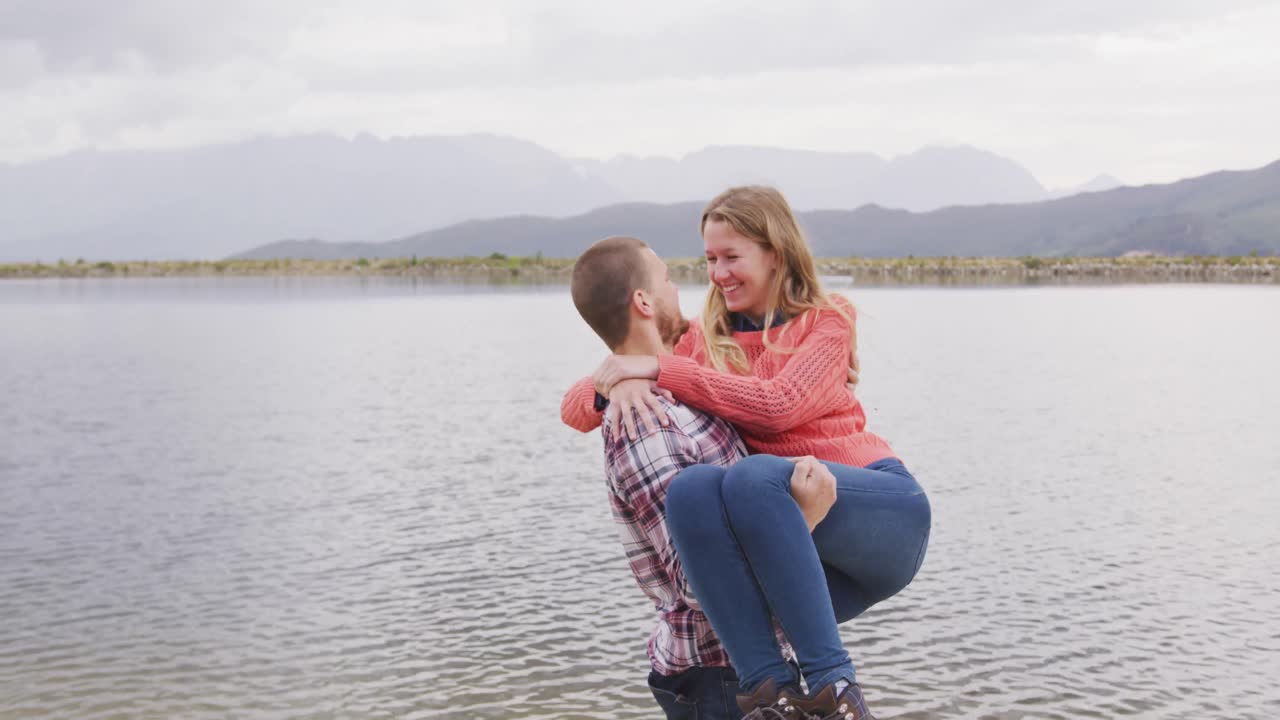 백인 부부가 산으로 여행하는 좋은 시간을 보내고, 미소 짓고, 남자가 여자를 들고 있습니다.