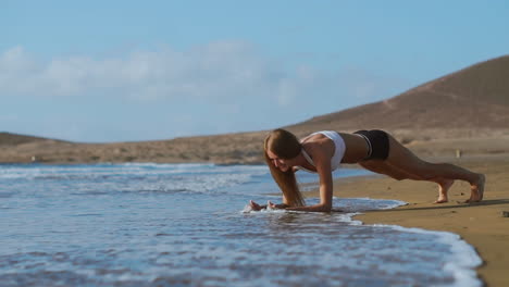 Vista-Lateral-De-Una-Hermosa-Mujer-Deportiva-En-Posición-De-Tabla-En-La-Playa-Durante-El-Atardecer.