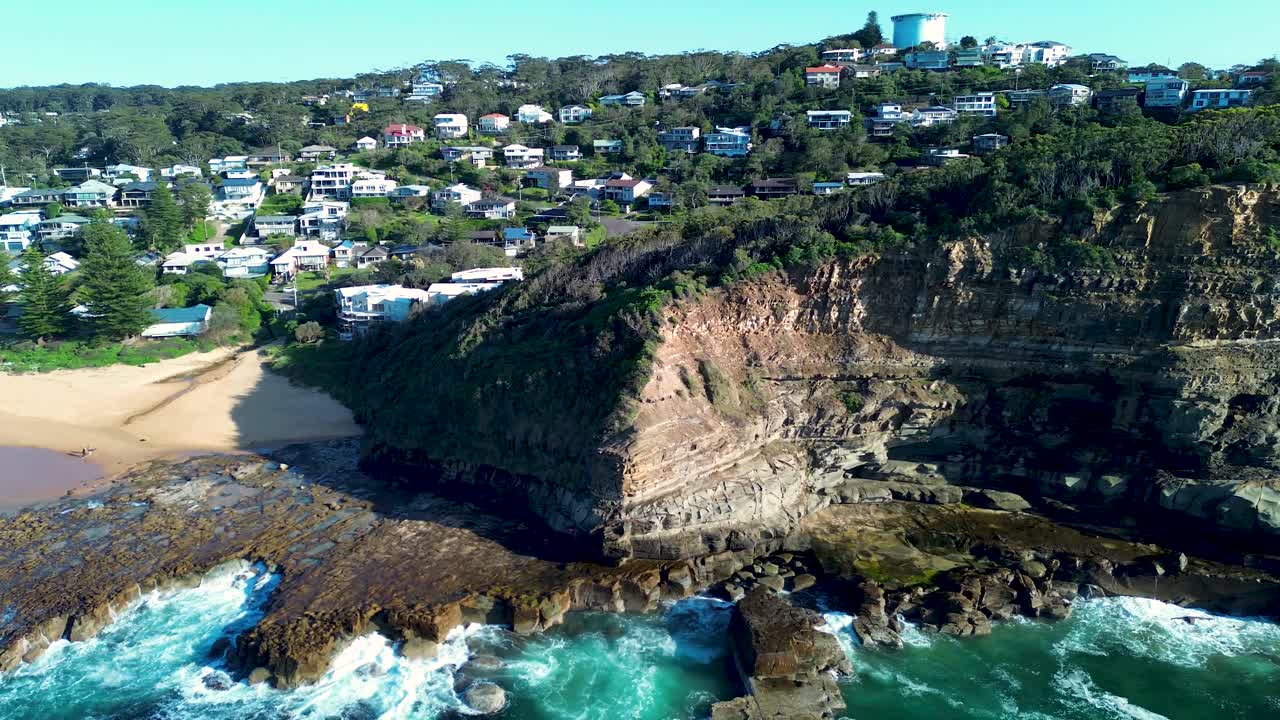 Drone aerial landscape of rugged headland cliffs at North Avoca Beach with ocean reef clear blue water and residential homes stretching along scenic coastline on Central Coast region Australia tourism