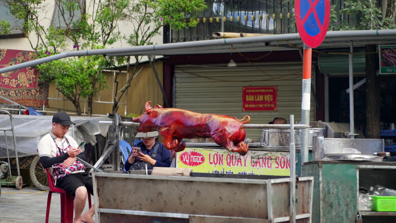 Wet market in Sapa, Vietnam, with locals vibrant red roast pork on spit in middle of market as vendor sits on phone