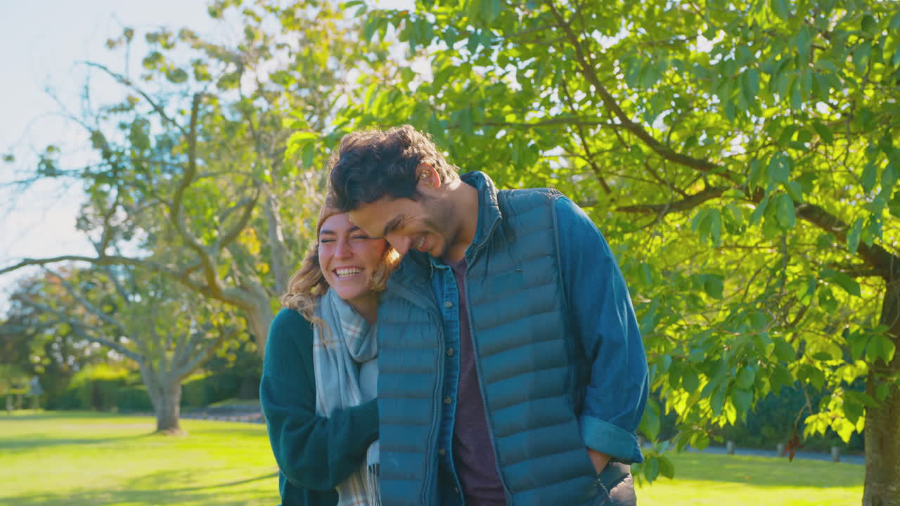 행복한 사랑하는 부부는 팔을 잡고 가을 공원을 걸어가면서 미소 짓고 있습니다.