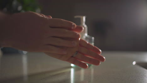 Man-reaches-into-frame-and-squirts-hand-sanitizer-into-his-hands-and-rubs-them-together