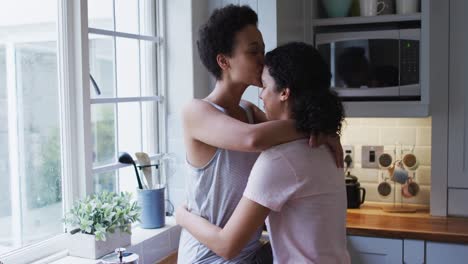 mixed race lesbian couple hugging and drinking coffee in kitchen