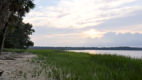 Glatter-Dolly-Von-Links-Nach-Rechts-Mit-Parallaxeneffekt-Auf-Gras-Im-Vordergrund,-Der-Einen-Küstensumpf-Bei-Sonnenuntergang-Mit-Wunderschönen-Farben-In-Den-Wolken-Und-Einer-Entspannenden-Atmosphäre-Enthüllt