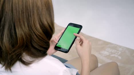 Young asian woman using black smartphone device with green screen. Asian woman mobile , scrolling pages while sitting on the couch in the living room. Chroma key.