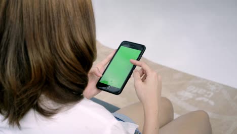 young asian woman using black smartphone device with green screen. asian woman mobile , scrolling pages while sitting on the couch in the living room. chroma key.