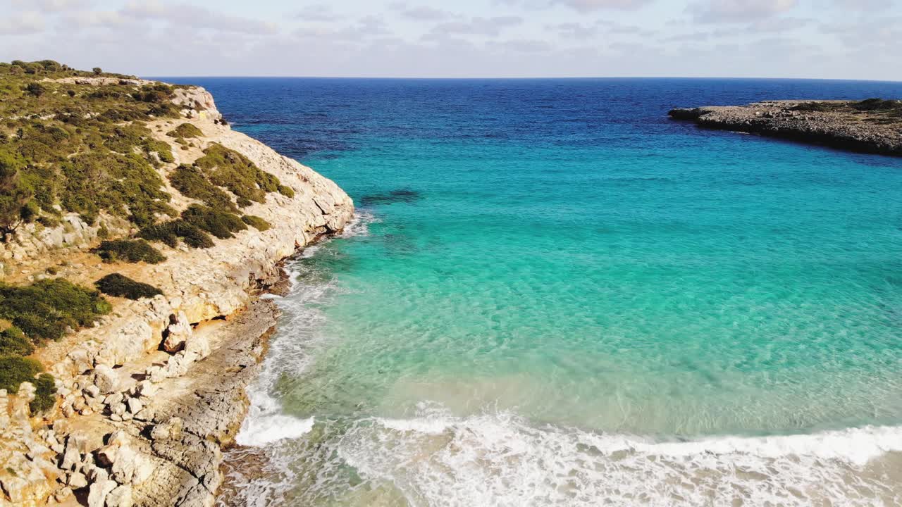 Una vasta ripresa aerea con drone che mostra la costa rocciosa di rocce di argilla rossa a Maiorca e poi la sabbia bianca della spiaggia e l'acqua blu del Mediterraneo