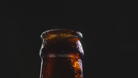 close up of condensation droplets on neck of revolving bottle of cold beer or soft drink with water vapour after opening 1