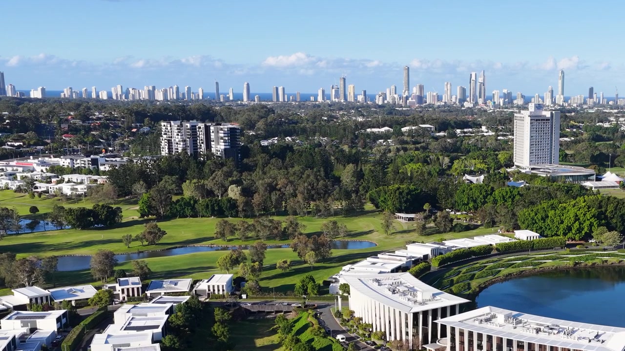 Ripresa aerea con drone di un resort di lusso, campo da golf e skyline cittadino in lontananza sotto la luce del sole.