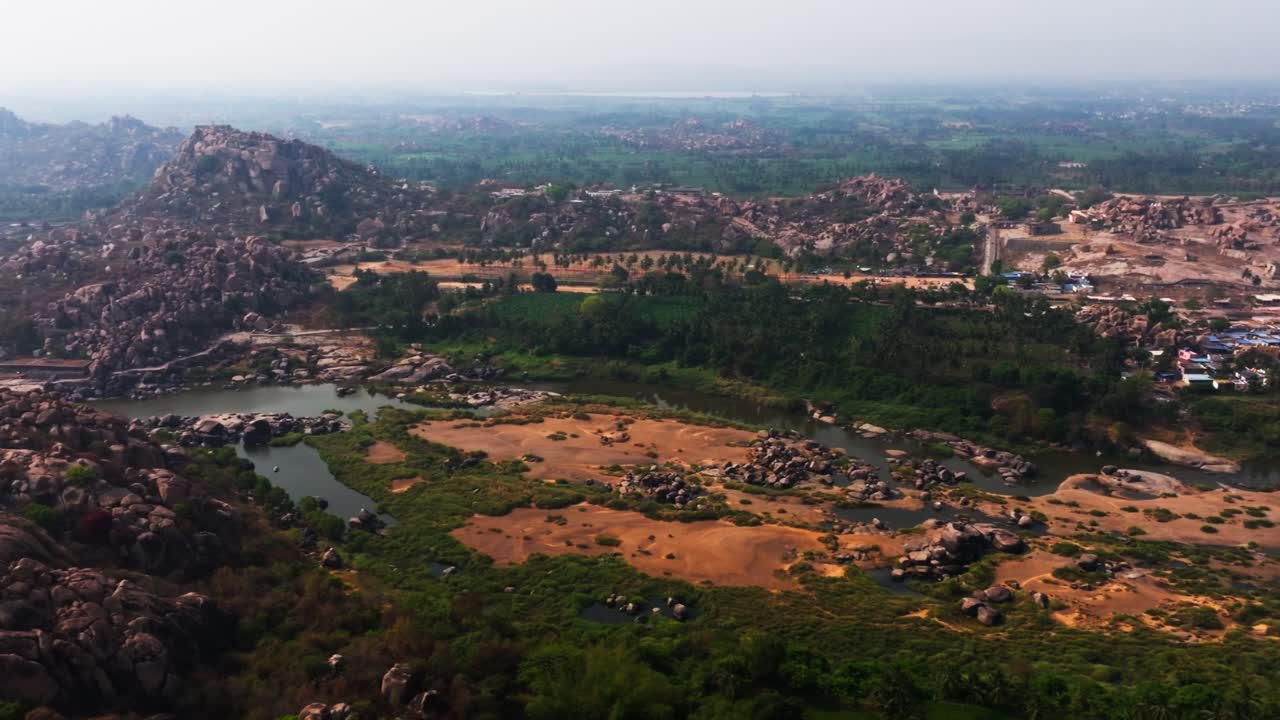 Lav vannføring i Tungabhadra-elven med fjell, grøntområder og Virupaksha-tempelet i Hampi, Karnataka, India. Dagtid, halvsirkel-opptak, dronebilde, 4k.