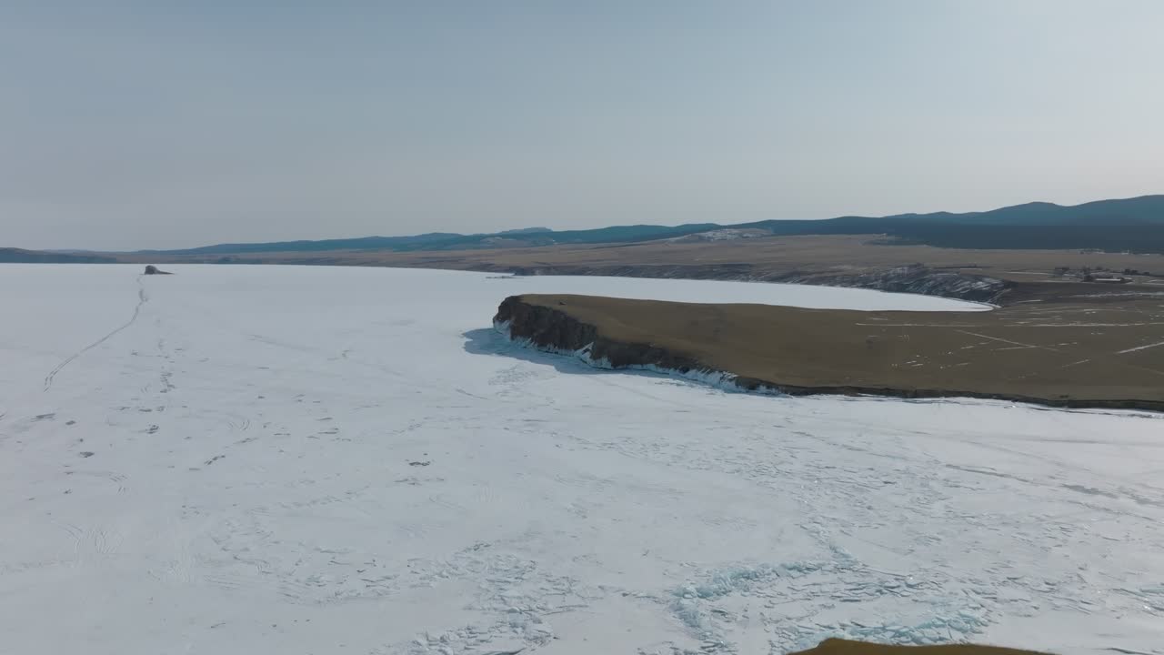 Droneoptagelser af den frosne kystlinje ved Kap Kharantsy på Olkhon-øen, Bajkalsøen, Rusland, med ismarker, klippefyldte skrænter og et vidtstrakt vinterlandskab.