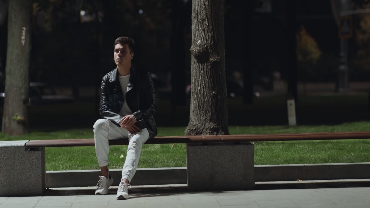 밤 에 벤치 에 앉아 있는 젊은 남자