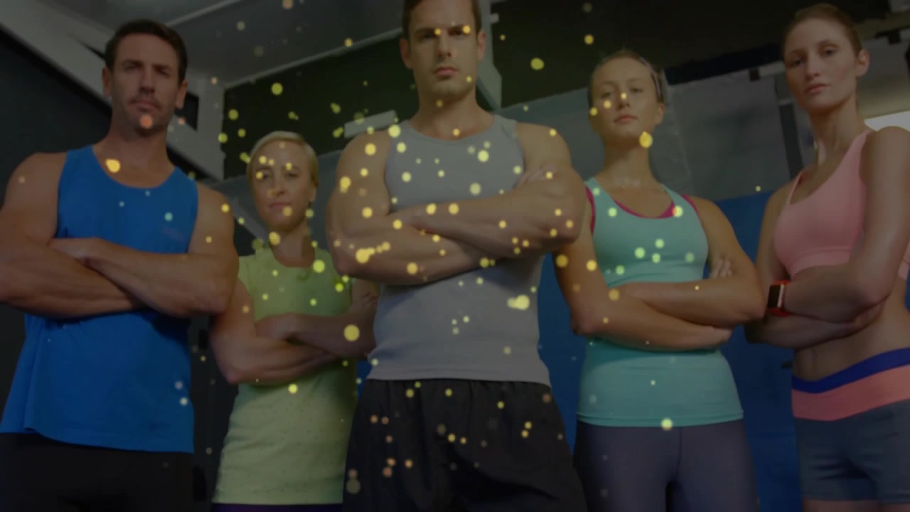Telecamera che si alza sopra una squadra di fitness con particelle dorate che fluttuano e l'allenatore centrale che lancia una sfida