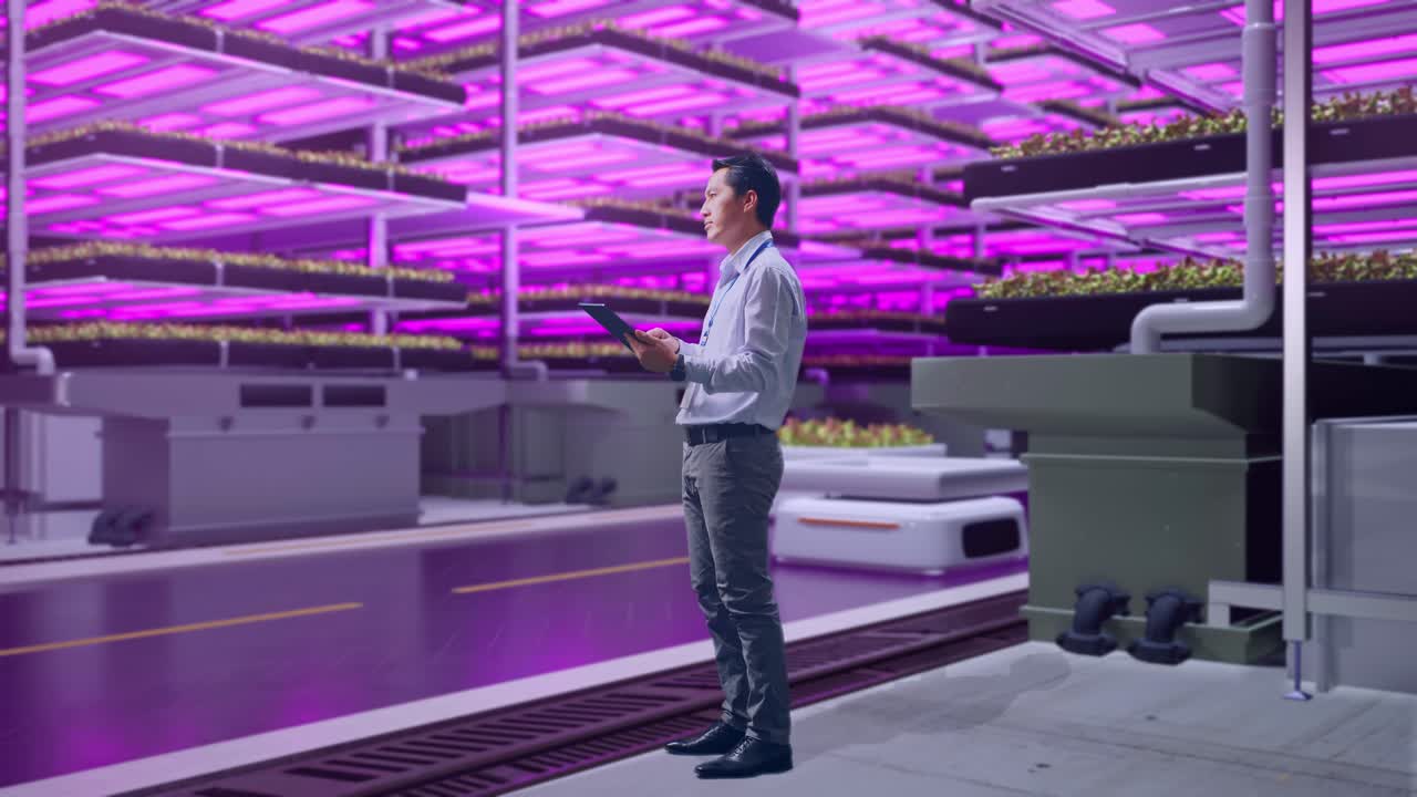 vista lateral del cuerpo completo de un trabajador profesional masculino asiático de pie con su tableta en una granja vertical, instalación industrial de alta tecnología, observa mirando a su alrededor antes de concentrarse con su tablet