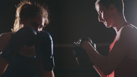 beautiful brunette boxer working out blows to the paws with a trainer in a dark room