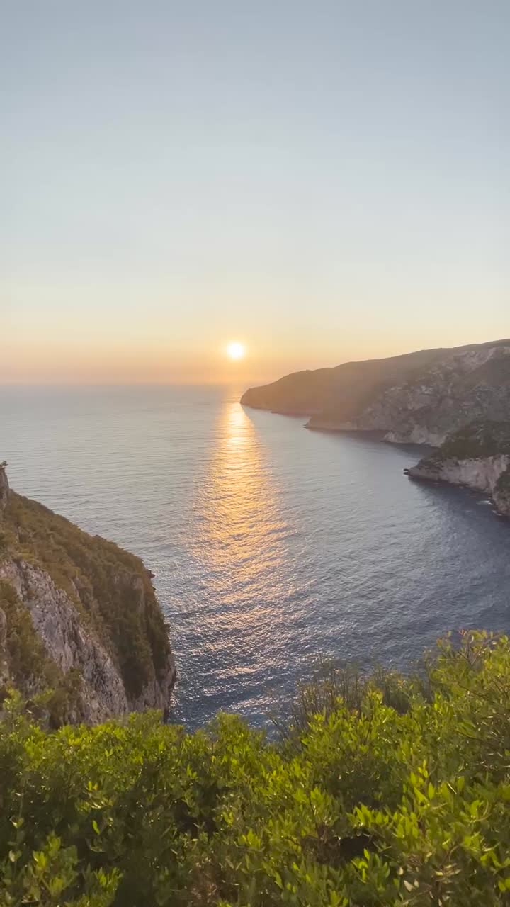 A beautiful view of the sunset from a cliff next to the water as the hill slop decreases towards the water.