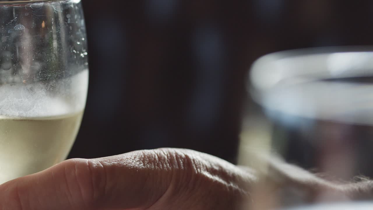 A close-up sequence shows a hand reaching for a cold white wine glass in a softly lit indoor setting, with shallow depth of field and gentle camera movement