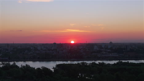beautiful sunset over a river with the city skyline silhouetted against the glowing sky.