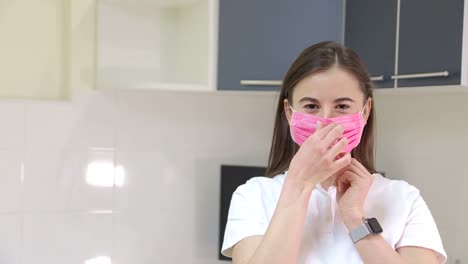 woman putting on a pink face mask in a kitchen