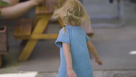 a little blonde-haired girl in a blue dress dances and spins joyfully