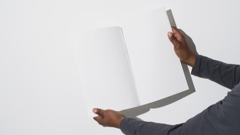 Video-of-hand-of-african-american-man-holding-book-with-blank-pages,-copy-space-on-white-background