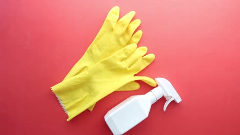 yellow cleaning gloves and spray bottle on red background