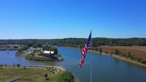 Orbit-drone-shot-of-a-American-flag-in-Clarksville-Marina-and-revealing-a-farmland-close-,-Tennesse