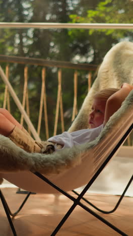 child leans on soft chair back at glamping. relaxed little boy enjoys recreation under glass dome on hotel terrace. kid spends happy summer holiday