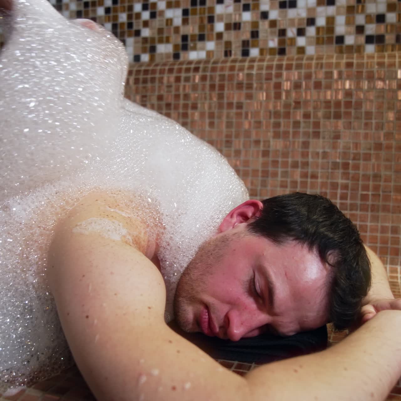 Foam massage procedure in the spa center. Man lies relaxed on the tiled bench while masseur applies soap foam on the customer