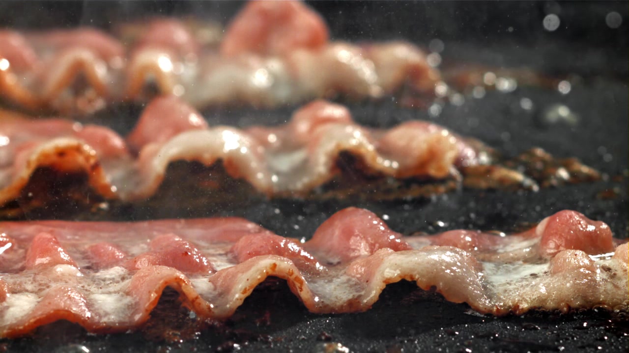 Primo piano di strisce di pancetta che sfrigolano in padella