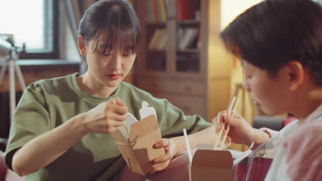 asian girlfriends eating wok from boxes and chatting at home