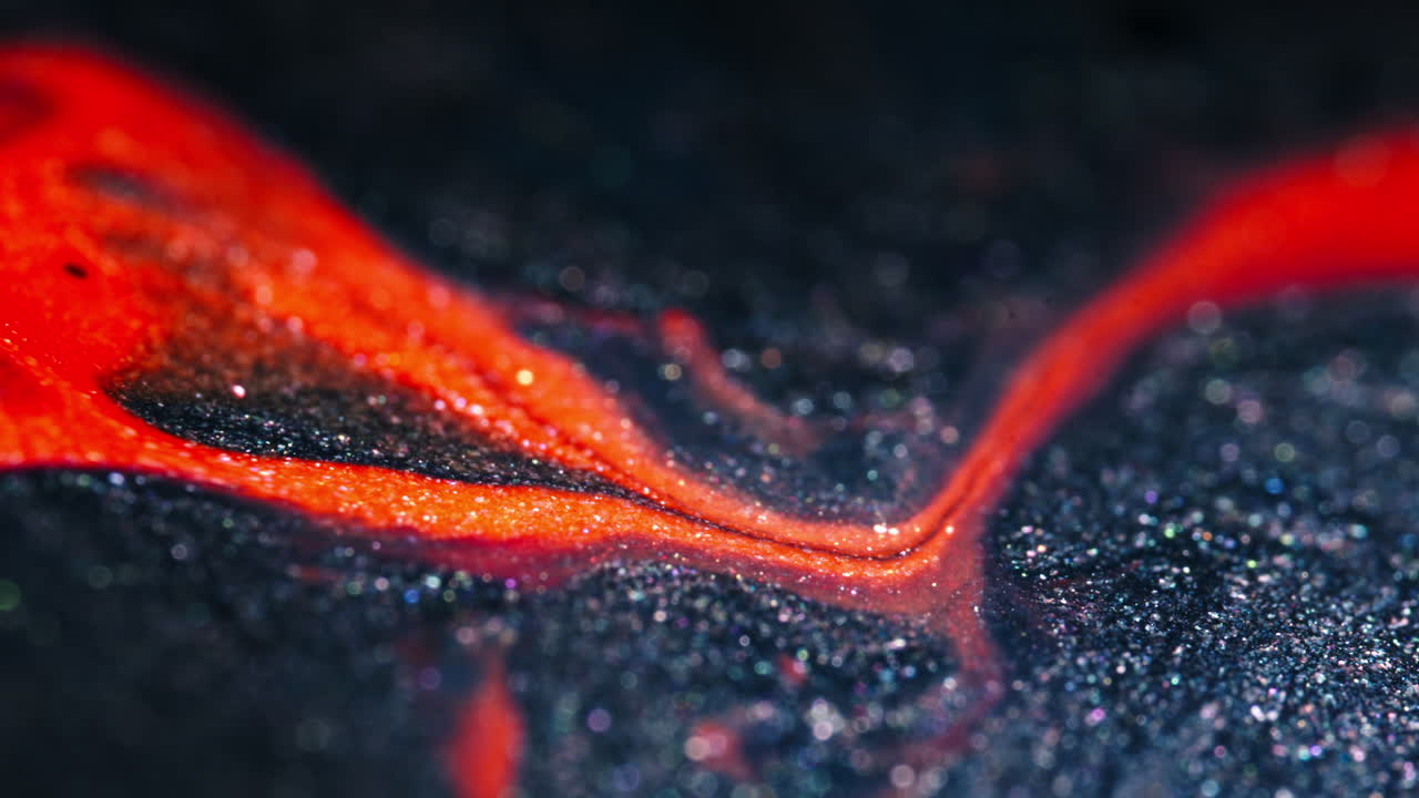 Molten red and black liquids swirl and blend in a mesmerizing macro shot with intense color contrast